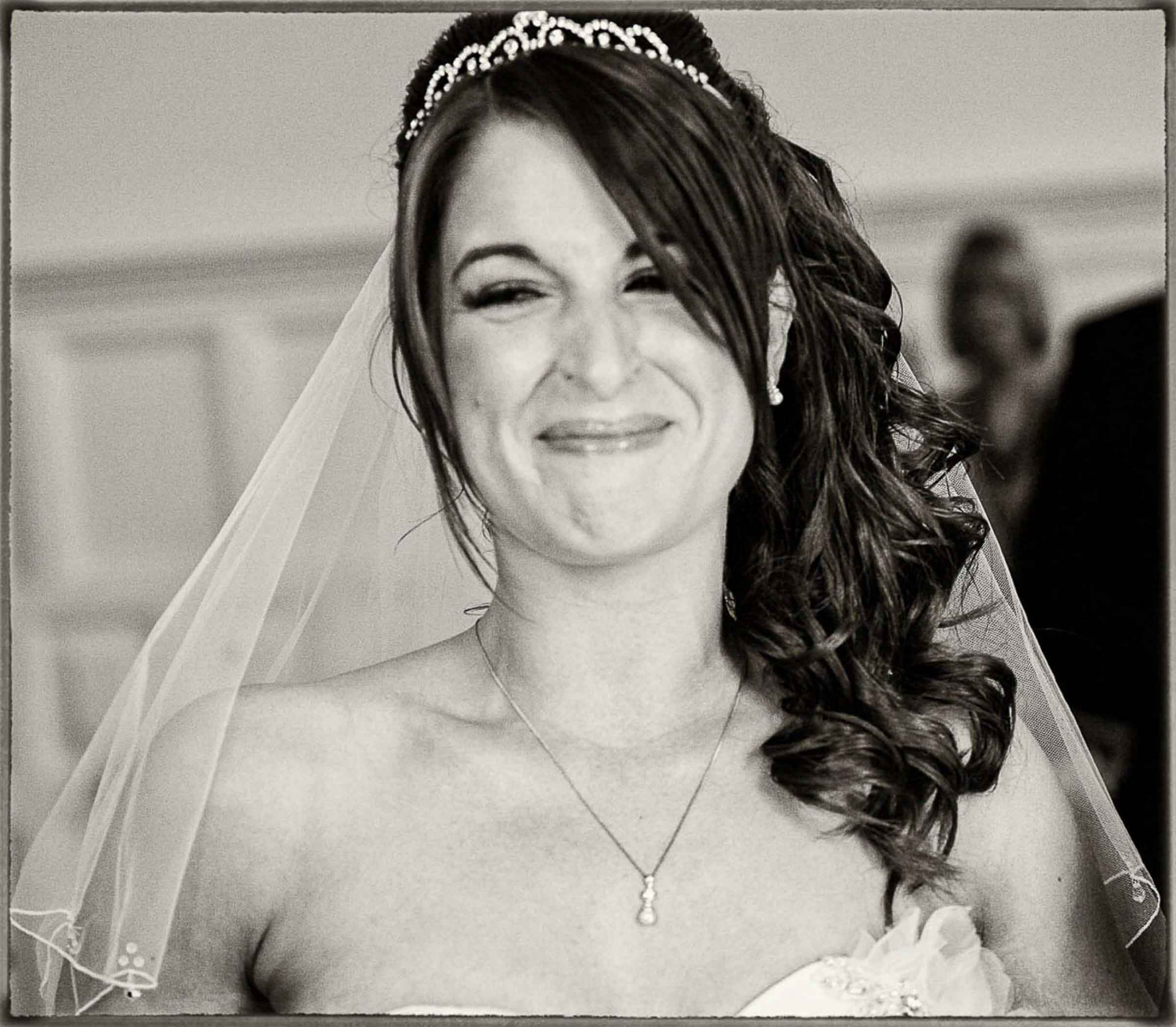 Black and white candid wedding photograph of a bride in a tiara and veil laughing