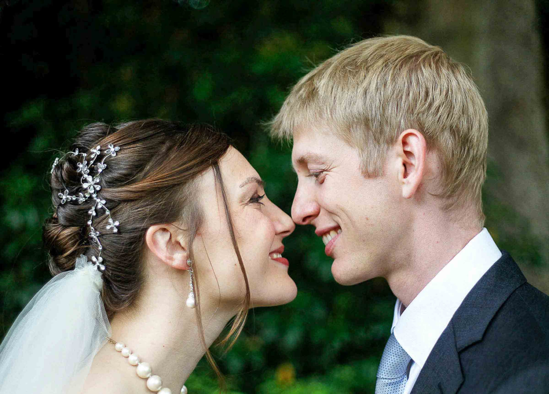 Bride and groom smiling forehead to forehead against green foliage at a Newport wedding