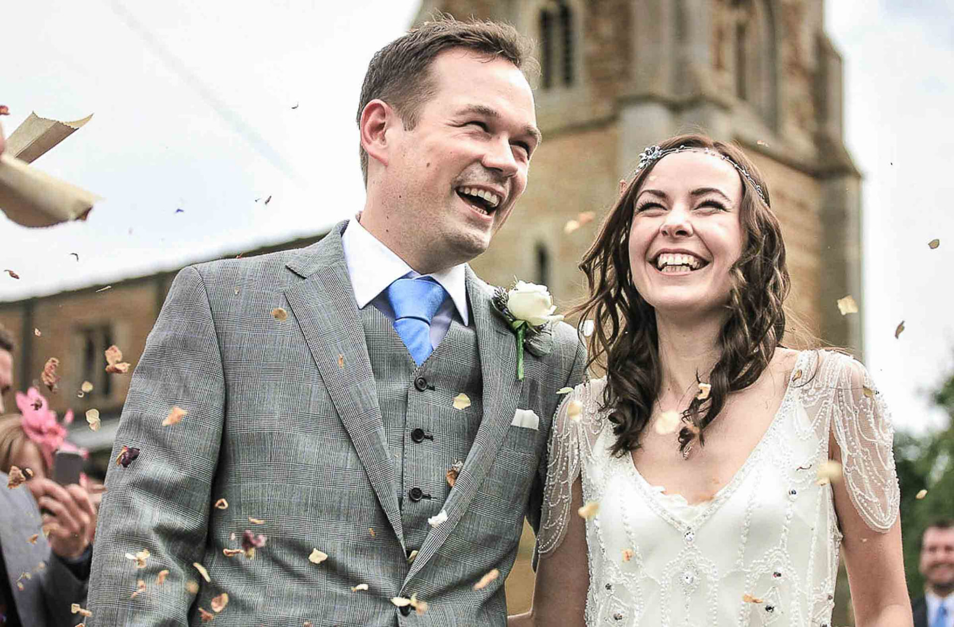 Bride and groom laughing as confetti falls outside a stone church in South Wales