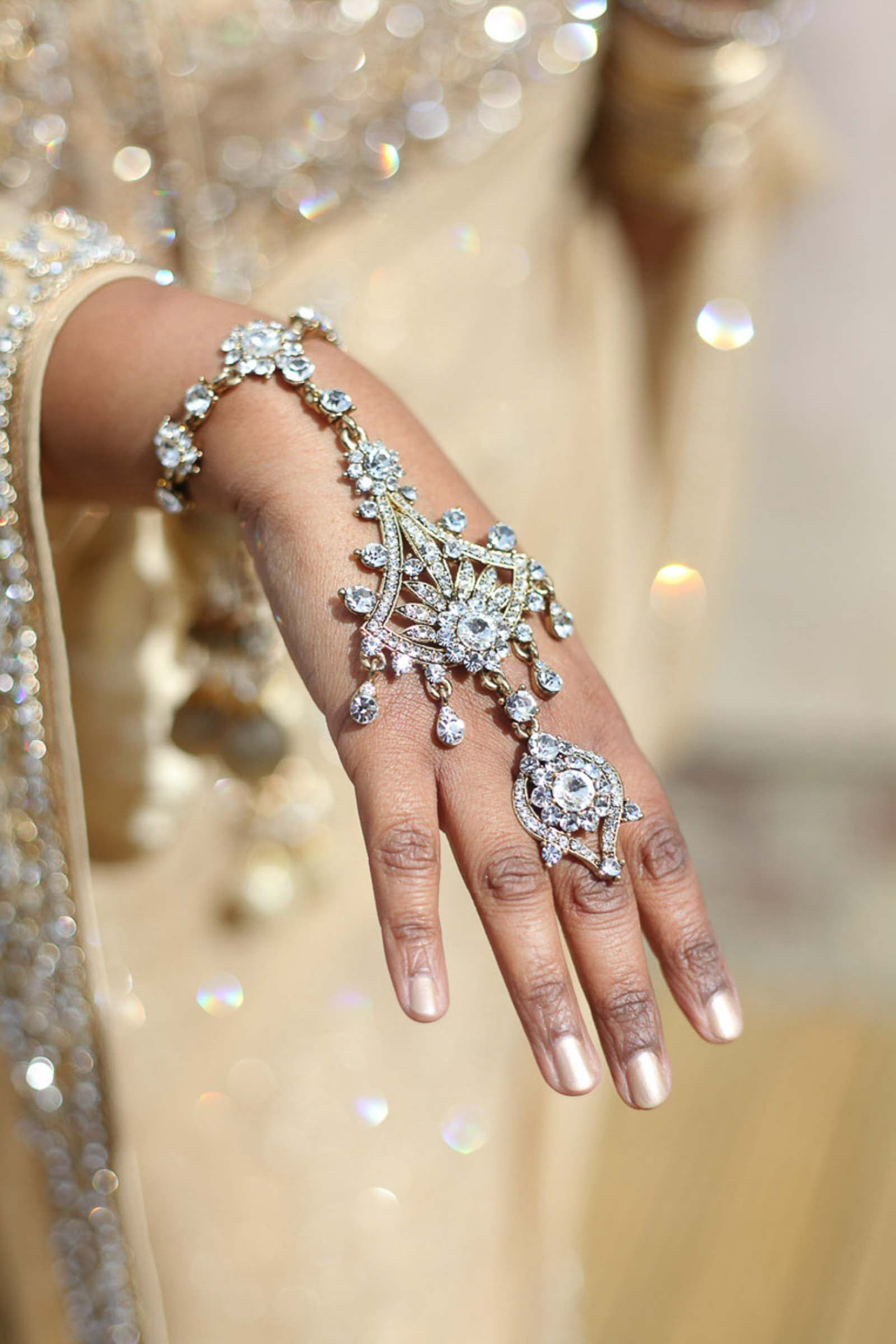 Close-up detail of a bride's crystal hand jewellery against gold bridal fabric