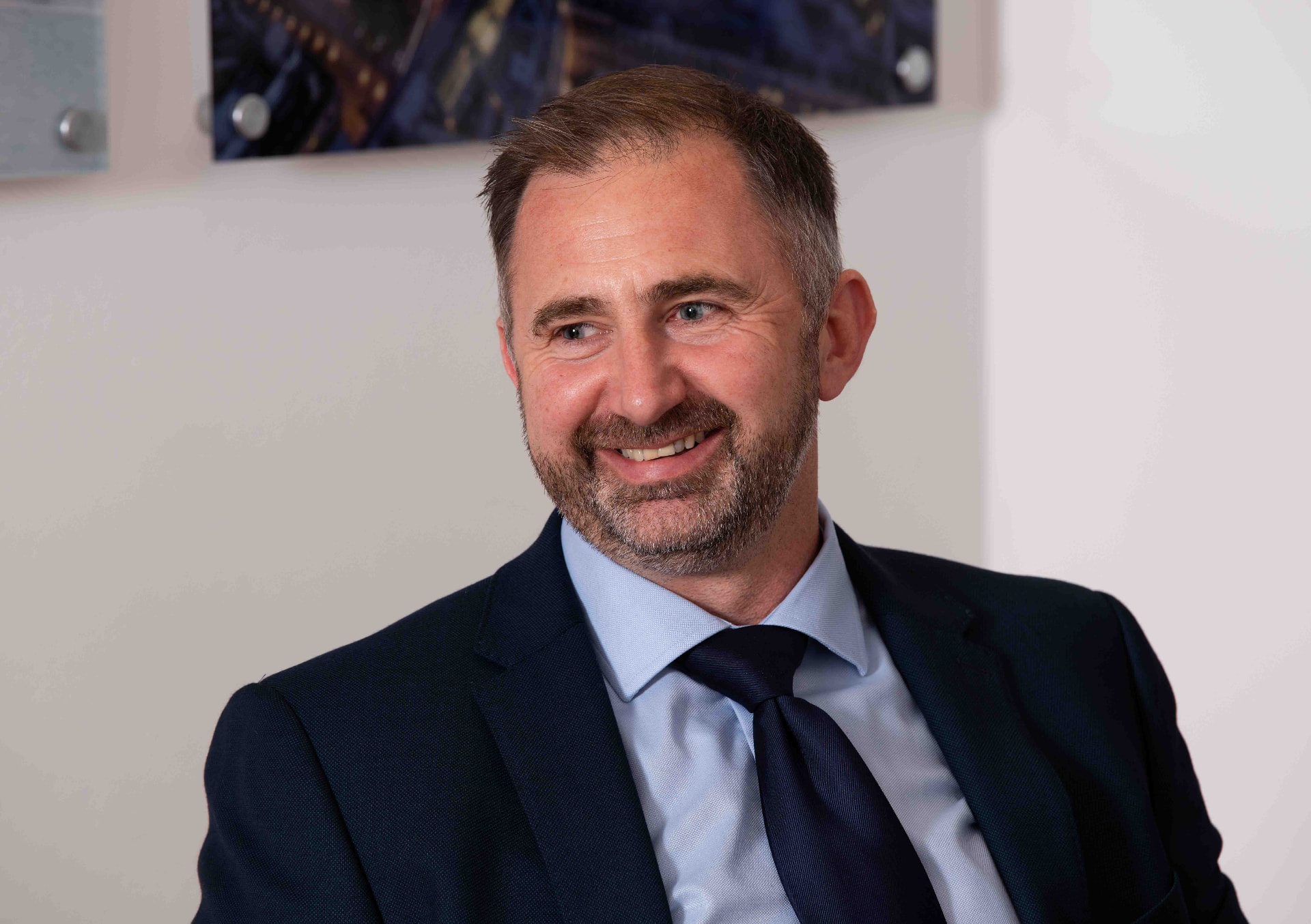 Corporate headshot of a smiling man in a navy suit in a bright Newport office