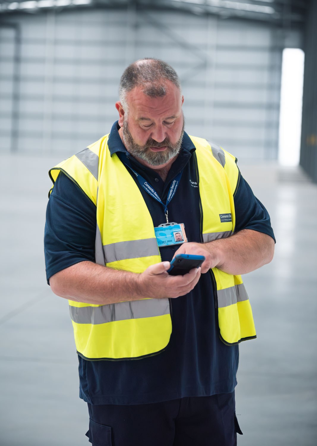 Security officer in a hi-vis vest checking his phone inside an empty warehouse, South Wales