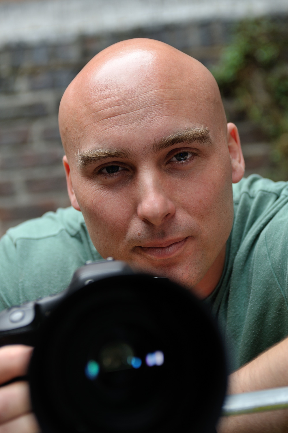 Jonathan, documentary photographer at Newport Photo Company, behind his camera against a brick wall