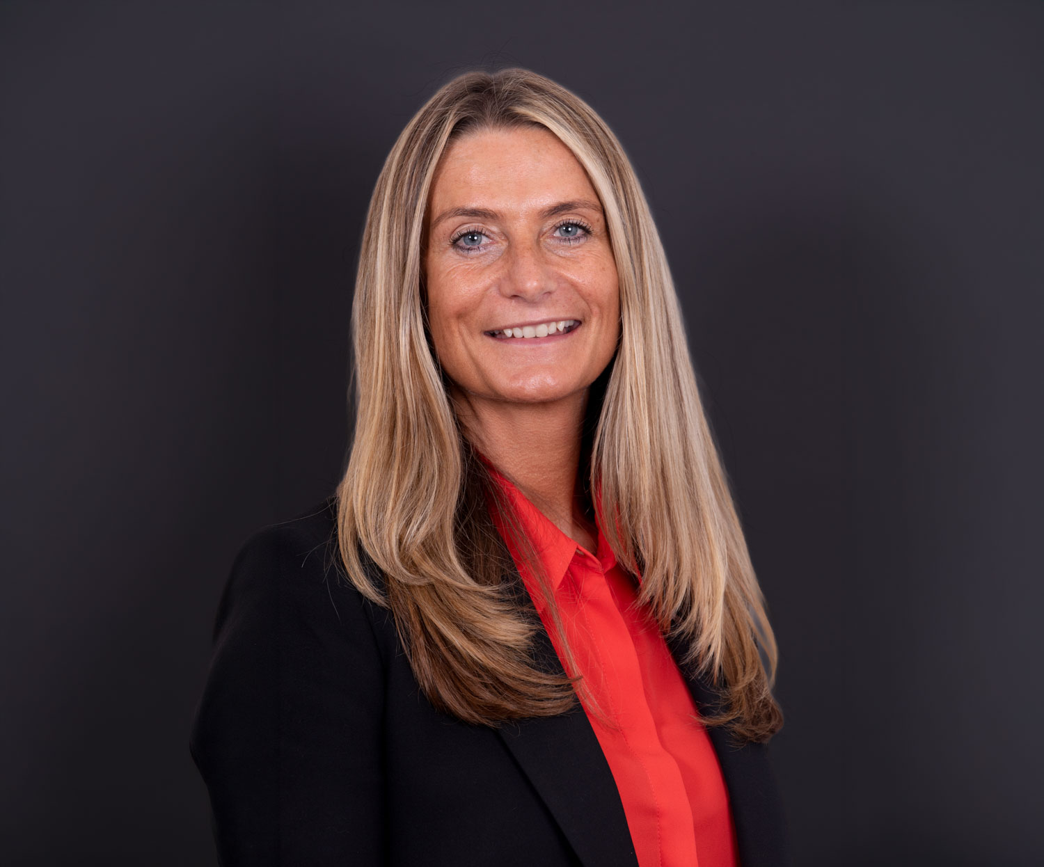 Corporate studio headshot of a smiling businesswoman in a black blazer and red shirt